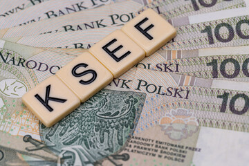 Blocks with the abbreviation KSEF, standing for National E-invoice System, are placed against a background of loosely spread Polish 100 PLN banknotes. The photo was taken under artificial lighting.
