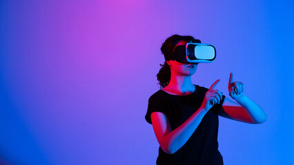 Woman using virtual reality headset and pointing at digital interface while interacting with immersive virtual space under neon lighting