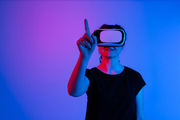 Woman in virtual reality headset raising finger and selecting virtual content against minimal neon background with copy space