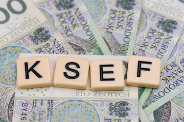 Blocks with the abbreviation KSEF, standing for National E-invoice System, are placed against a background of loosely spread Polish 100 PLN banknotes. The photo was taken under artificial lighting.
