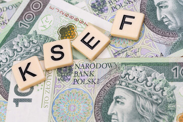Blocks with the abbreviation KSEF, standing for National E-invoice System, are placed against a background of loosely spread Polish 100 PLN banknotes. The photo was taken under artificial lighting.