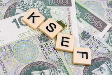 Blocks with the abbreviation KSEF, standing for National E-invoice System, are placed against a background of loosely spread Polish 100 PLN banknotes. The photo was taken under artificial lighting.
