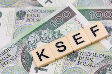 Blocks with the abbreviation KSEF, standing for National E-invoice System, are placed against a background of loosely spread Polish 100 PLN banknotes. The photo was taken under artificial lighting.
