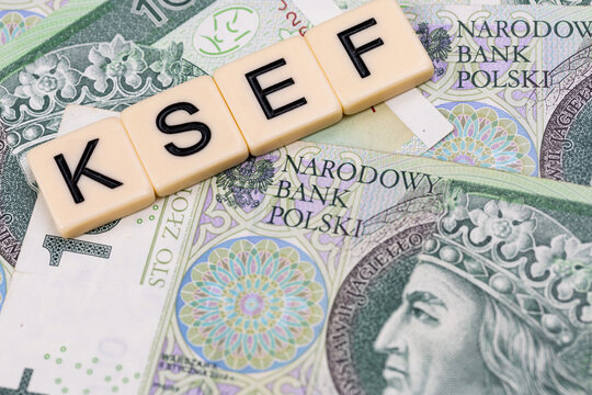 Blocks with the abbreviation KSEF, standing for National E-invoice System, are placed against a background of loosely spread Polish 100 PLN banknotes. The photo was taken under artificial lighting.