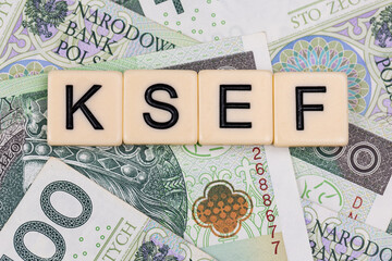 Blocks with the abbreviation KSEF, standing for National E-invoice System, are placed against a background of loosely spread Polish 100 PLN banknotes. The photo was taken under artificial lighting.
