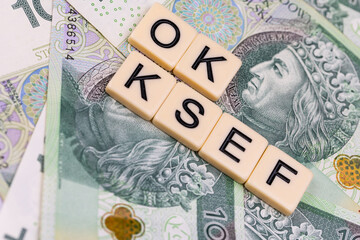 Blocks with the abbreviation OK KSEF, standing for positives about National E-invoice System, are placed against a background of loosely spread Polish 100 PLN banknotes. 