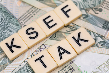 Blocks with the abbreviation TAK KSEF, standing for positives about National E-invoice System, are placed against a background of loosely spread Polish 100 PLN banknotes. 