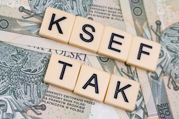 Blocks with the abbreviation TAK KSEF, standing for positives about National E-invoice System, are placed against a background of loosely spread Polish 100 PLN banknotes. 