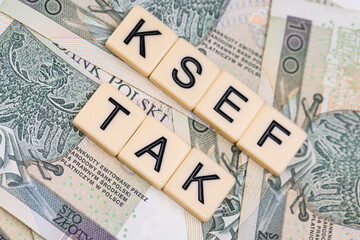 Blocks with the abbreviation TAK KSEF, standing for positives about National E-invoice System, are placed against a background of loosely spread Polish 100 PLN banknotes. 