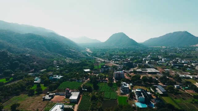 Aerial view of the landscape, showcasing verdant rolling hills and a dense cityscape with buildings, trees, and fields, Pushkar, Rajasthan, India.