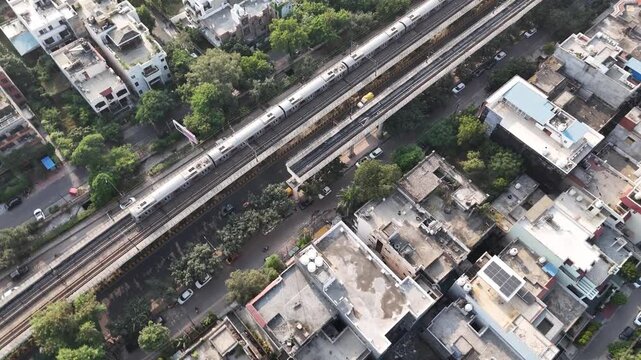 Top-down aerial view of a Delhi Metro train gliding along elevated tracks above dense residential neighborhoods, highlighting urban mobility woven into everyday city life.