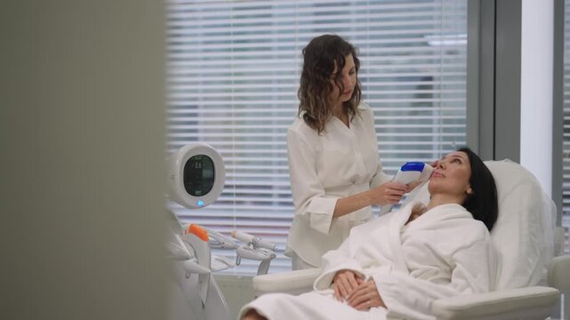 Tracking shot of cosmetologist performing ultrasound facial lifting treatment on woman face in beauty clinic, focusing on skin rejuvenation and anti-aging care. Concept of facial antiaging treatment.