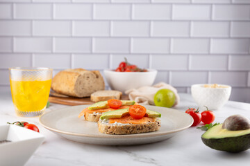 Minimalist composition of a healthy breakfast with salmon, avocado and tomato toasts on a beige plate. Fresh ingredients and drink in soft background. Concept of balanced diet and clean eating