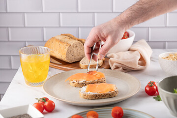 Healthy Cooking Process: Male Hands Garnishing Toast with Smoked Salmon. Fresh ingredients on marble countertop. Great for mindful eating content or organic food marketing