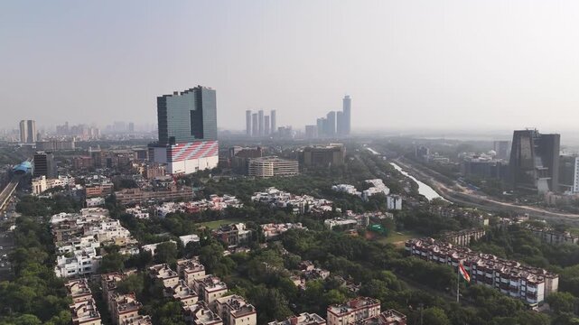 Wide aerial view of Noida&rsquo;s urban skyline with modern high-rise towers rising above green residential neighborhoods, seen under a light haze that reflects NCR&rsquo;s air pollution and rapid growth.