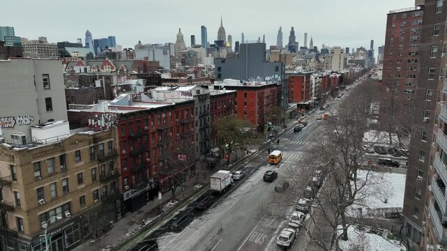 Drilling cars on yellow school buses on Main Street of american suburb neighborhood in New York city. Snowy winter day with Manhattan skyline in background. Aerial descend wide shot.