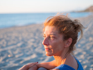 Thoughtful woman at seaside during golden hour in Calabria, portrait on sandy beach with soft light, calm mood, solitude, reflection, coastal lifestyle, southern Italy