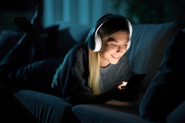 Happy woman wearing headphone using phone in the night