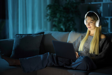 Satisfied woman wearing headphone in the night at home using laptop
