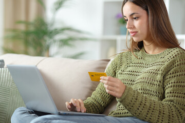 Serious woman in gren paying online with computer on a sofa