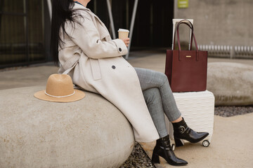 Woman in coat sitting with luggage and coffee