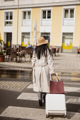Woman with rolling suitcase crossing urban street 