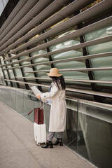 Traveler checking map near modern building with luggage