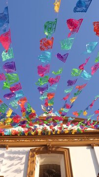 Vibrant papel picado waving from a building against a blue sky.