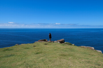 A woman stands at a view point overlooking the ocean
