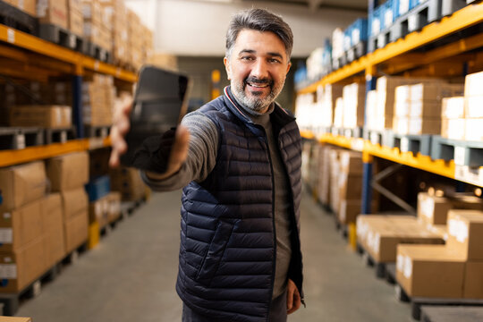 Warehouse worker holding smartphone blank screen mockup. Logistics manager using app for inventory tracking. Digital transformation in industry and supply chain background. - Powered by Adobe