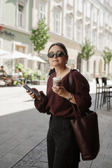 Woman walking with coffee and smartphone in city