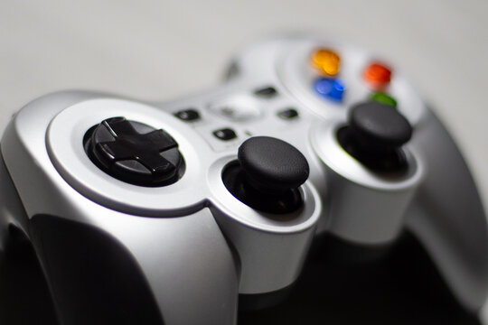 Manette de jeu vid&eacute;o en gros plan, avec joysticks noirs analogiques, boutons directionnel D-pad et touches color&eacute;es (bleu, rouge, jaune, vert) sur fond blanc minimaliste, pr&ecirc;t pour gaming intensif.