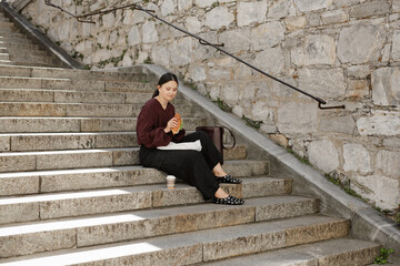 Woman Eating Sandwich Sitting on Outdoor Stone Steps