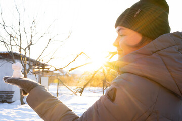 woman holds a duck-shaped figure made of snow in her hand, conspiracy games, cold season