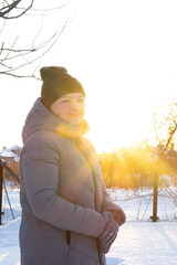 portrait of a woman at sunset in warm clothes, jacket and hat, cold winter, snow all around and sun rays