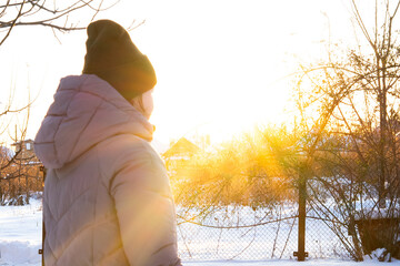 portrait of a woman at sunset in warm clothes, jacket and hat, cold winter, snow all around and sun rays