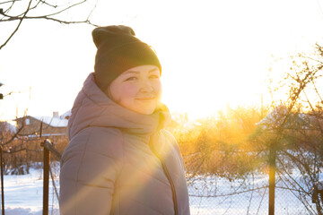 portrait of a woman at sunset in warm clothes, jacket and hat, cold winter, snow all around and sun rays