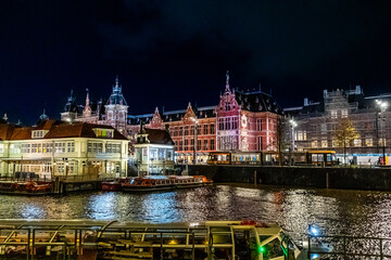 Amsterdam Railway station canal water house building. Netherlands night. Evening street architecture. Water boats