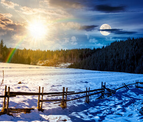 rustic wooden fence through snow covered hill. day and night time change concept. beautiful view in winter mountains with sun and moon. alpine rural landscape near forest. equality and shift template