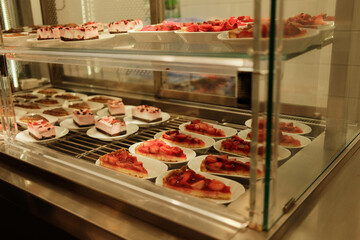 Strawberry cheesecake slices arranged on plates inside a bakery display case. Fresh fruit dessert concept for cafe menu and pastry showcase.