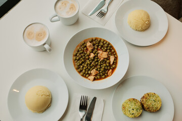 Top view of a lunch table with green pea stew and chicken, mashed potatoes, vegetable patties and coffee cups. Balanced home style meal concept, simple cafeteria food.