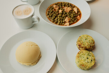 Close view of green pea stew with chicken pieces served on white plates with mashed potatoes and vegetable patties. Warm homemade lunch concept, casual dining atmosphere.