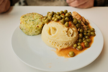 Mashed potatoes topped with green pea stew and chicken pieces on a white plate. Simple comfort food dish, homemade lunch concept with vegetables and protein.