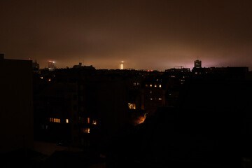 Night view of residential apartment buildings with glowing windows under an overcast sky. Urban neighborhood atmosphere with warm city lights, quiet evening mood and dense housing skyline.