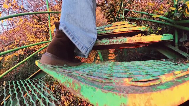 Climbing stairs outdoors person in denim jeans and boots ascending an old weathered green metal staircase in a sunny park at sunset
