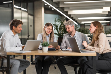 Successful businesspeople working in a coworking space working with laptop discussing strategy and business plan in modern office.