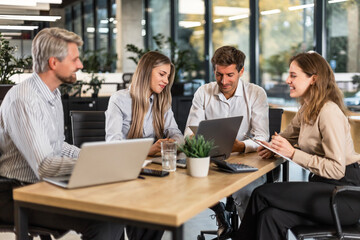 Group of confident business people in smart casual wear working together while sitting at the desk in office