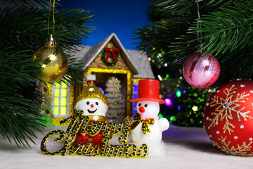 Between two balls on the Christmas tree branches there are two snowmen and a larger ball against the background of a house