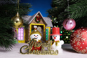 Two snowmen with letters between Christmas trees against the backdrop of a Christmas house
