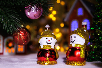 Two identical snowmen between Christmas trees against the backdrop of Christmas houses